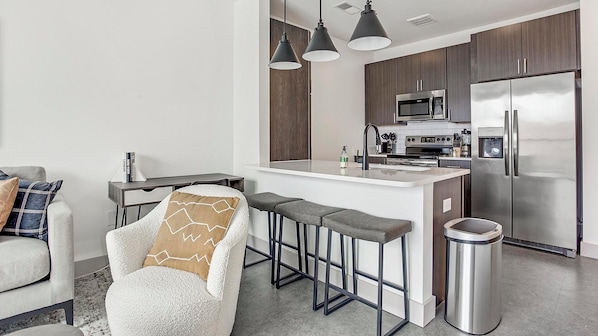A modern kitchen with a central island, bar stools, a stainless steel refrigerator, and a microwave. - Landing | Incredible 1BD, Gym, Pool (Richmond)