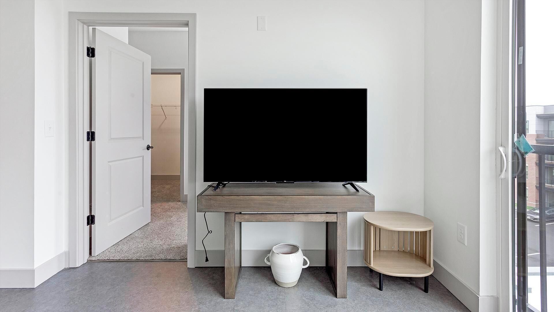 Een kamer met een televisie op een houten standaard, een kleine witte vaas en een gebogen houten plank.