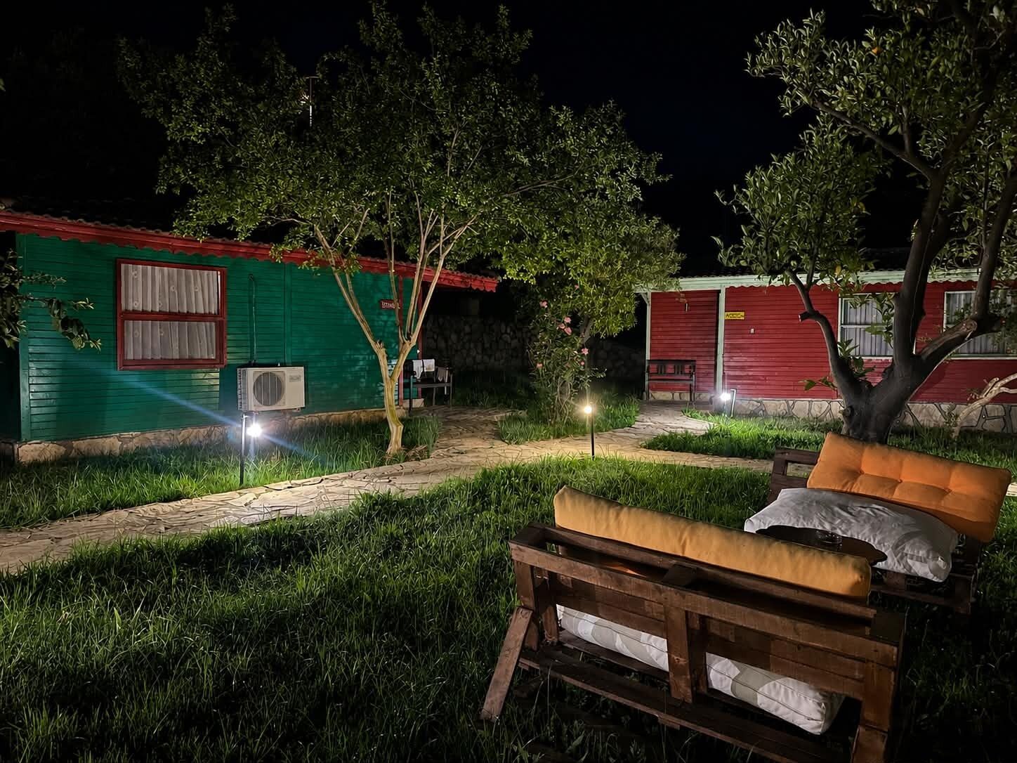A nighttime outdoor area with a wooden bench, a pathway, and two red buildings with green walls.