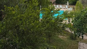 Una piscina con sillas de descanso, rodeada de árboles y una colina al fondo.