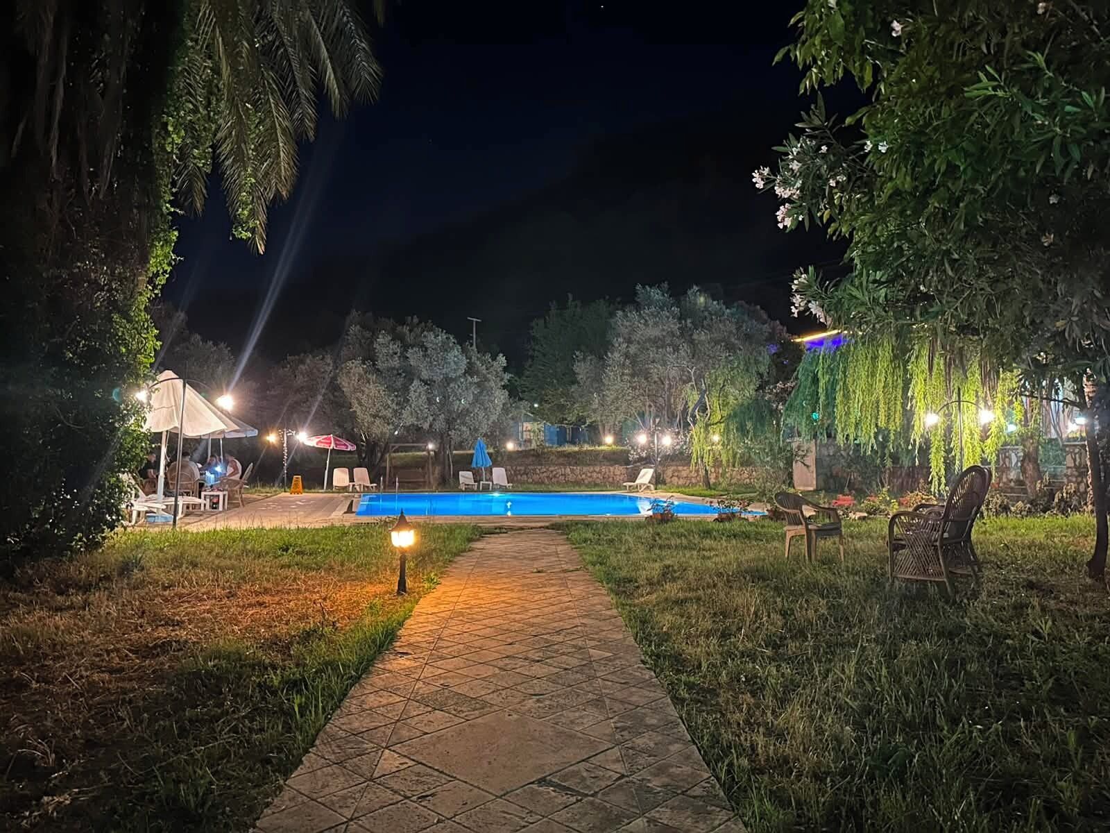 A nighttime outdoor pool area with a tiled pathway, lounge chairs, and ambient lighting.