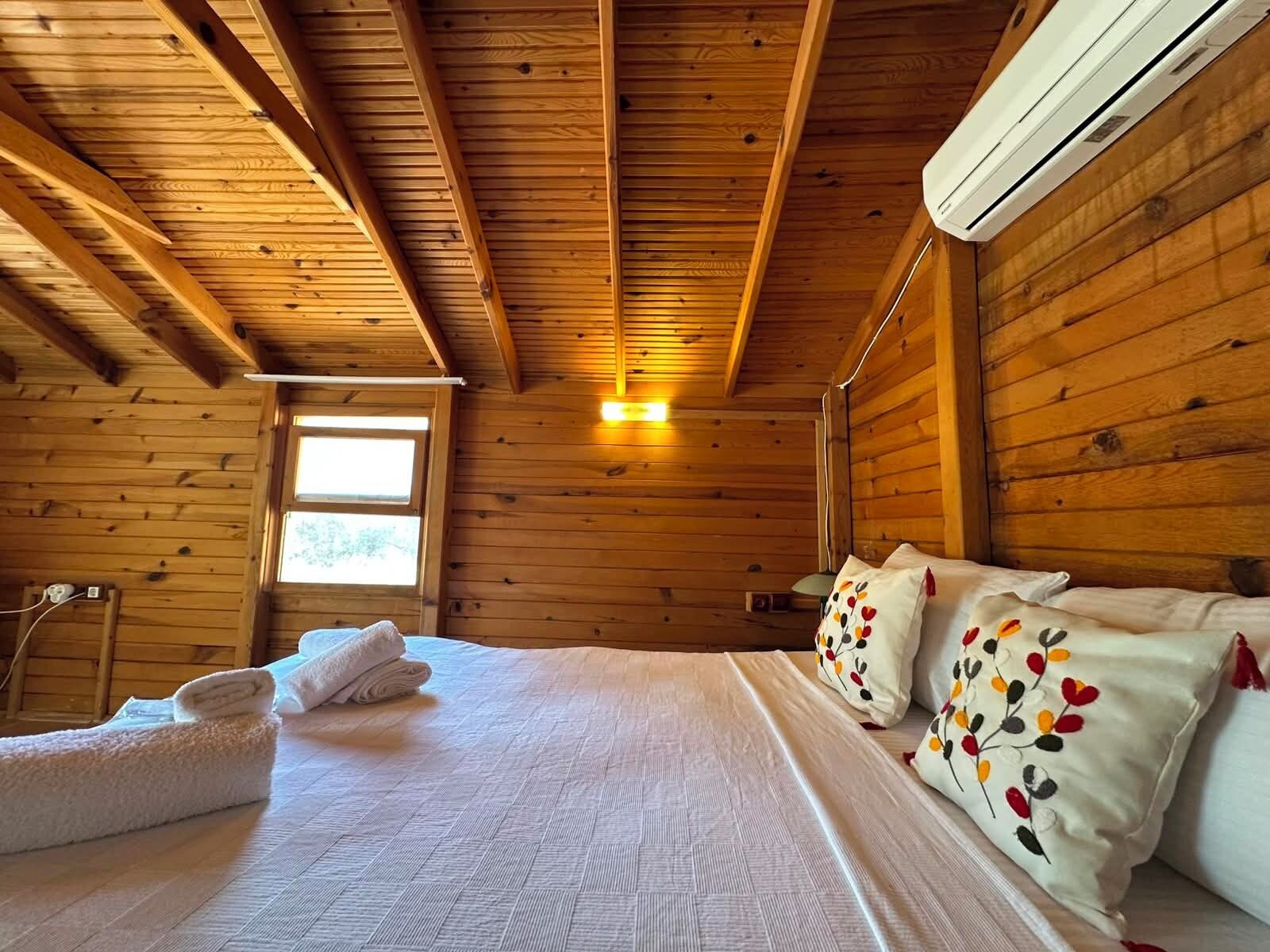 Dormitorio de cabaña de madera con cama, almohadas y ventana.