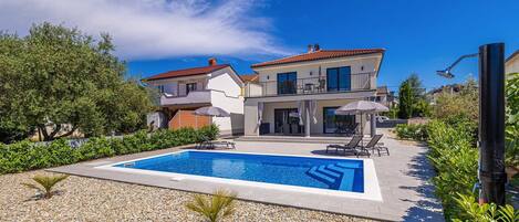 Una casa de dos pisos con piscina y zona de estar exterior.
