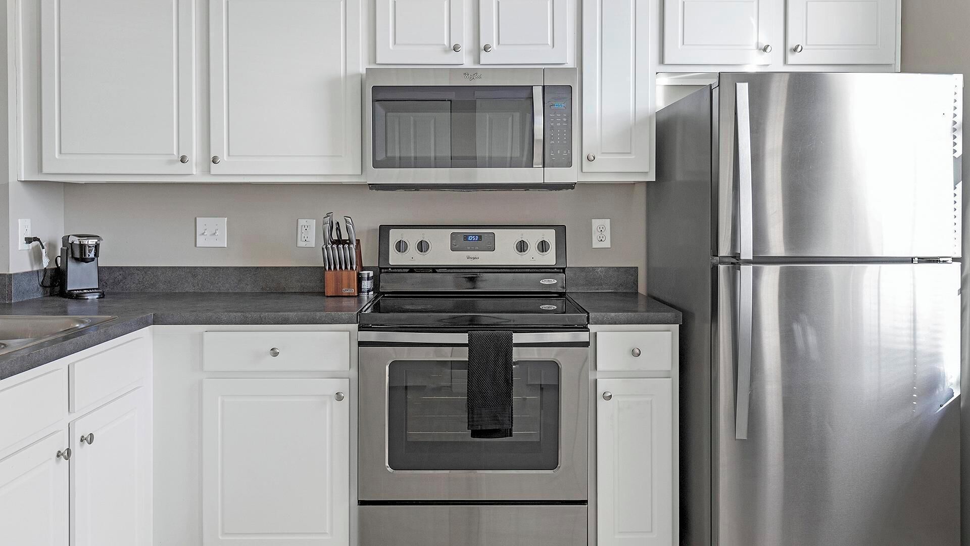 A kitchen with white cabinets, a stainless steel refrigerator, a microwave, and an oven.