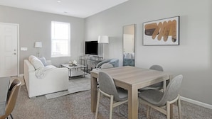 Een moderne woonkamer met een bank, salontafel, televisie en een eethoek.