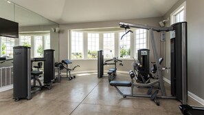 Ein Fitnessstudio mit verschiedenen Trainingsgeräten, großen Fenstern und einer Spiegelwand.