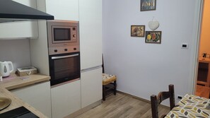 Et kompakt køkken med mikrobølgeovn, ovn og et lille spiseområde med stol og bord.