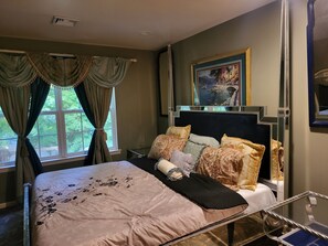 Quarto com cama, cortinas, um quadro e um espelho.