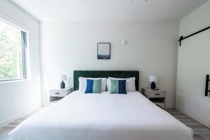 Ein Hotelzimmer mit einem großen Bett, zwei Nachttischen mit Lampen, einem Blick ins Freie durch ein Fenster und einem Gemälde an der Wand.