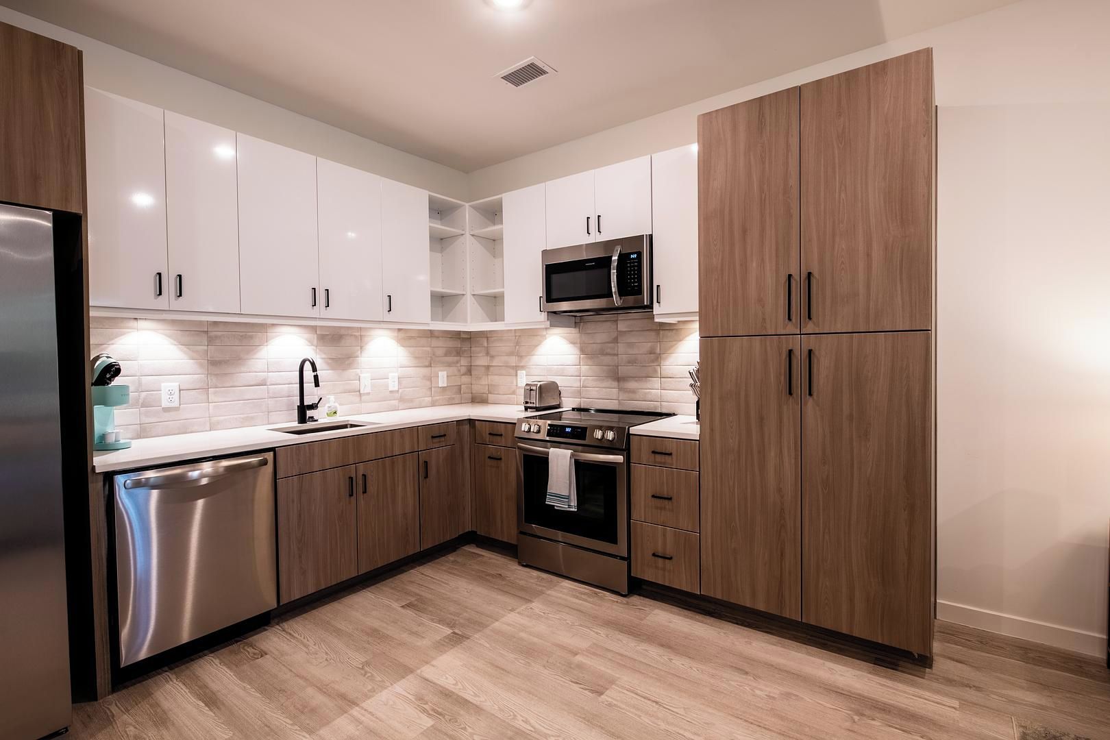 A modern kitchen with white cabinets, a stainless steel dishwasher, a microwave, and a stove.