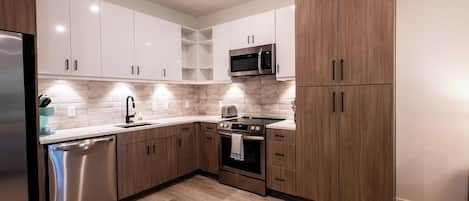 A modern kitchen with white cabinets, a stainless steel dishwasher, a microwave, and a stove.