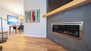 Een moderne woonkamer met een open haard, houten vloeren en eigentijdse kunstwerken.