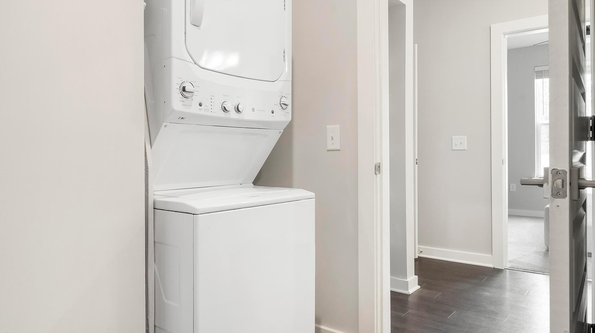 Une buanderie équipée d’un lave-linge et d’un sèche-linge à chargement frontal, d’une porte donnant sur une autre pièce et d’un interrupteur sur le mur.