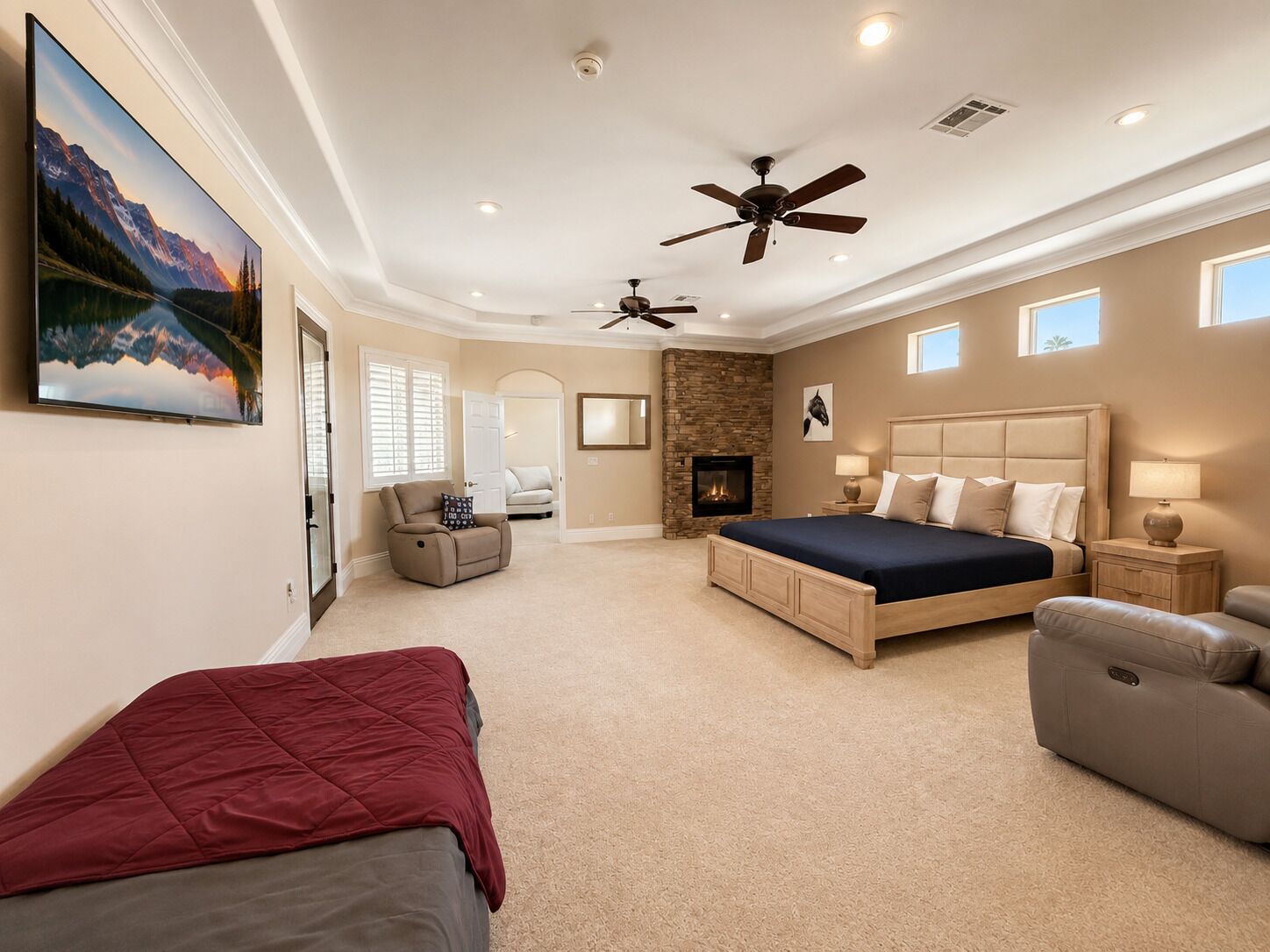 A bedroom with a large bed, a fireplace, a ceiling fan, and a painting on the wall.