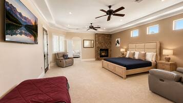 A bedroom with a large bed, a fireplace, a ceiling fan, and a painting on the wall.