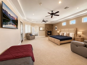 A bedroom with a large bed, a fireplace, a ceiling fan, and a painting on the wall. - Exquisite 9BR/5BA Villa - Sports Court, Game Room, Movie Room, Pool, & Spa ★★★★★ (North Las Vegas)