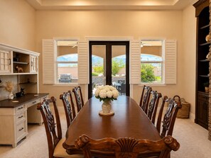 A dining room with a long wooden table, white chairs, and a vase of flowers. - Exquisite 9BR/5BA Villa - Sports Court, Game Room, Movie Room, Pool, & Spa ★★★★★ (North Las Vegas)