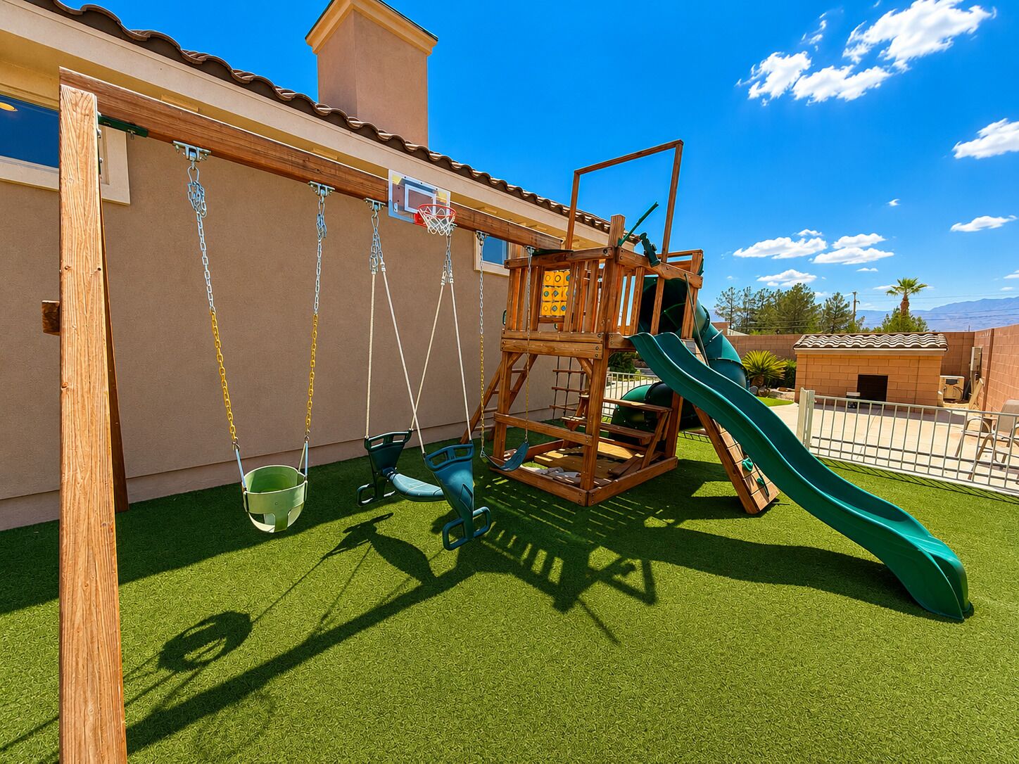 A wooden play structure with swings and a slide, set on artificial grass.