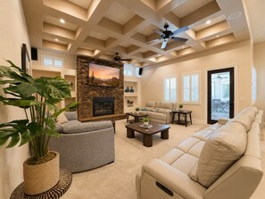 A living room with a stone fireplace, a ceiling fan, and a large window.