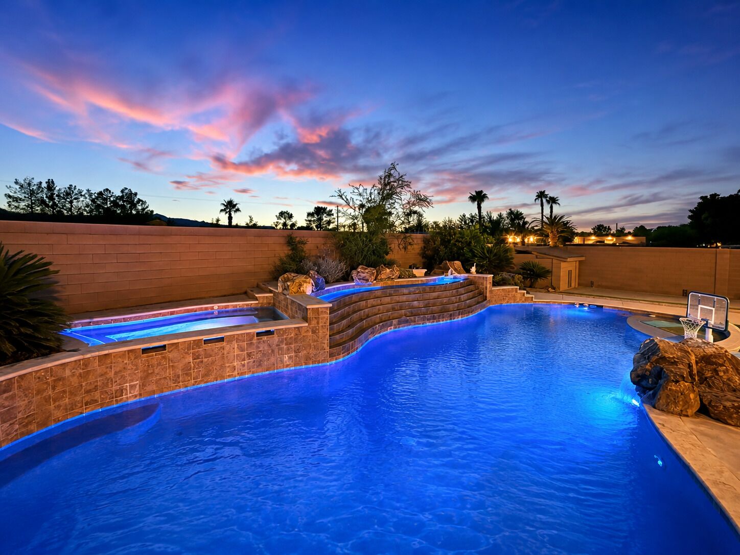 A swimming pool with a built-in hot tub and a basketball hoop.