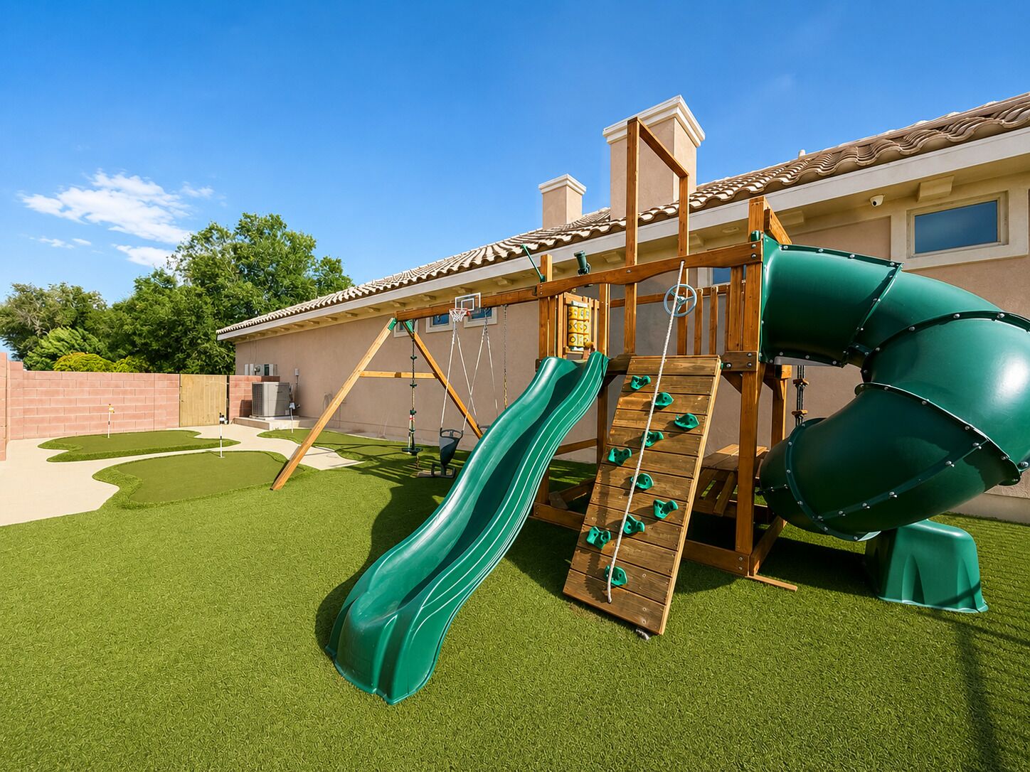 A playground with a slide and climbing area, surrounded by a house and a brick wall.
