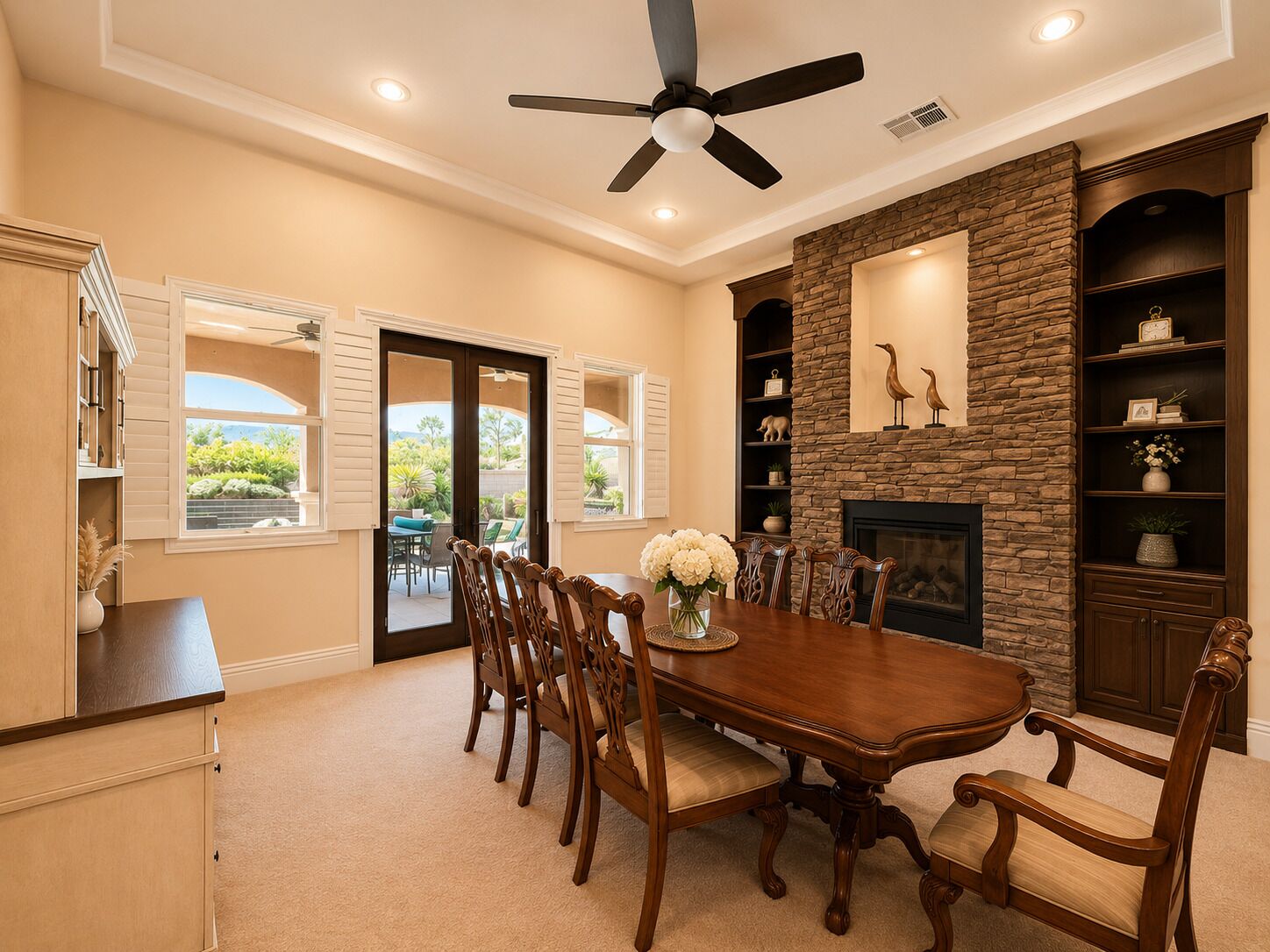 A dining room with a large table, chairs, a ceiling fan, and a stone fireplace.