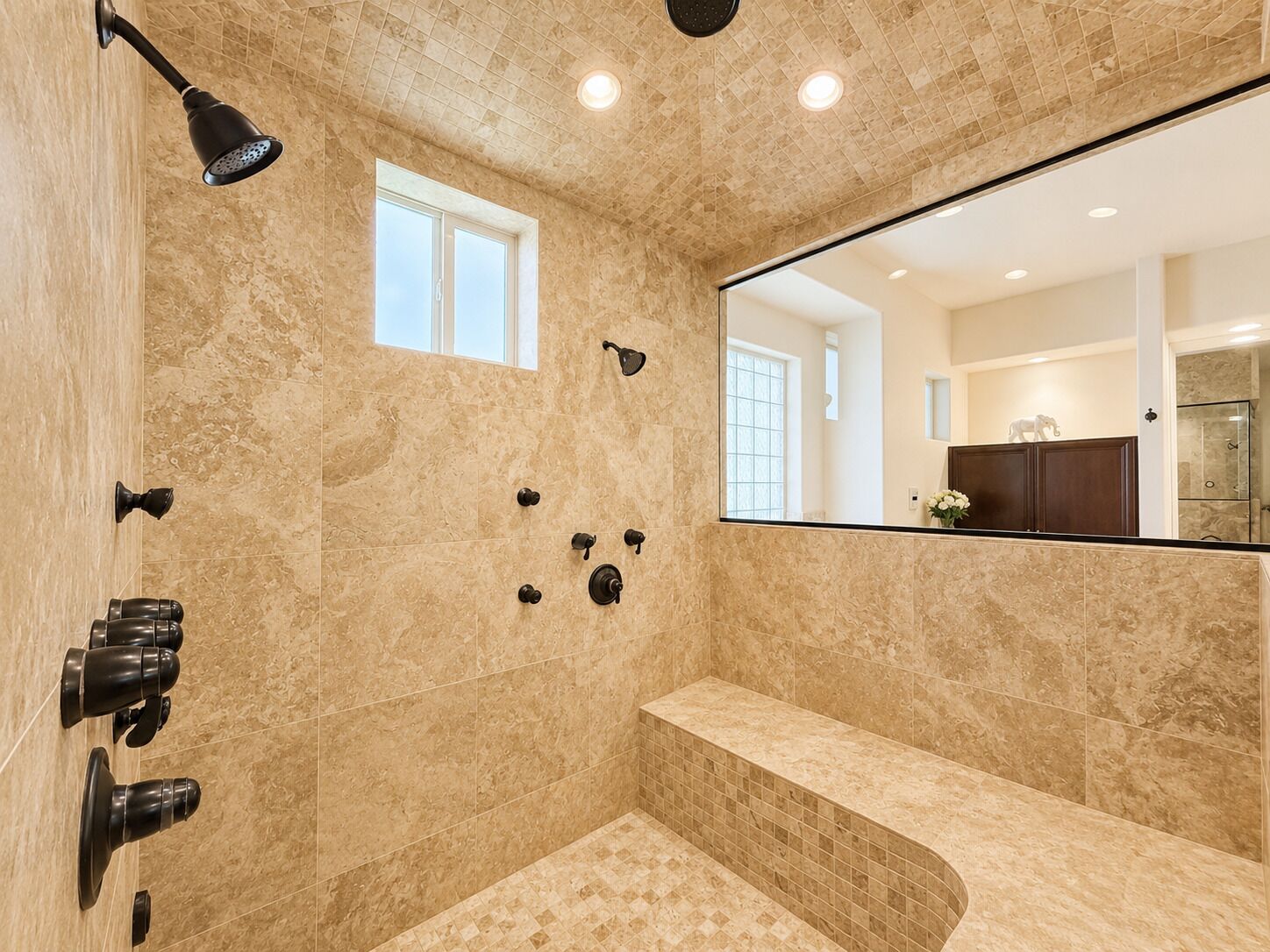 A bathroom with a large mirror, a shower with multiple controls, and a bench.