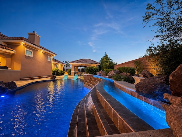 A swimming pool with a curved design, surrounded by a landscaped area with rocks and plants.