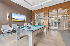 Een pooltafel met stoelen, een televisie toont een mooi uitzicht, en een modern interieur met houten lambrisering en glazen deuren.