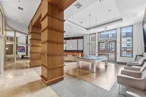 A modern hotel lobby with a pool table, seating area, and large windows offering views. - Landing | Incredible 2BD, Gym, Clubhouse (Bayonne)
