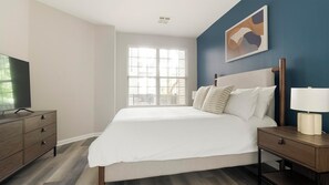 A hotel room with a bed, bedside tables, a TV, and a window with blinds. - Landing | Incredible 2BD, Gym, Clubhouse (Bayonne)
