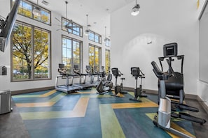 A gym with treadmills, elliptical machines, and a stationary bike, large windows, and a colorful floor. - Landing | Incredible 2BD, Gym, Clubhouse (Bayonne)