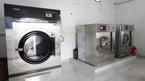 Un cuarto de lavandería con dos lavadoras industriales, un extintor y suelo de baldosas.