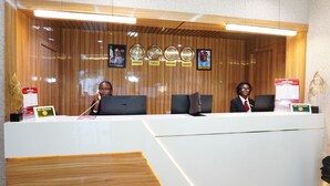 Un mostrador de recepción con un panel de madera en la pared, un cartel de 'No Fumar' y relojes que muestran diferentes husos horarios.