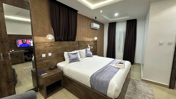 Una habitación de hotel moderna con una cama grande, una mesita de noche, un espejo, un televisor y un aire acondicionado.