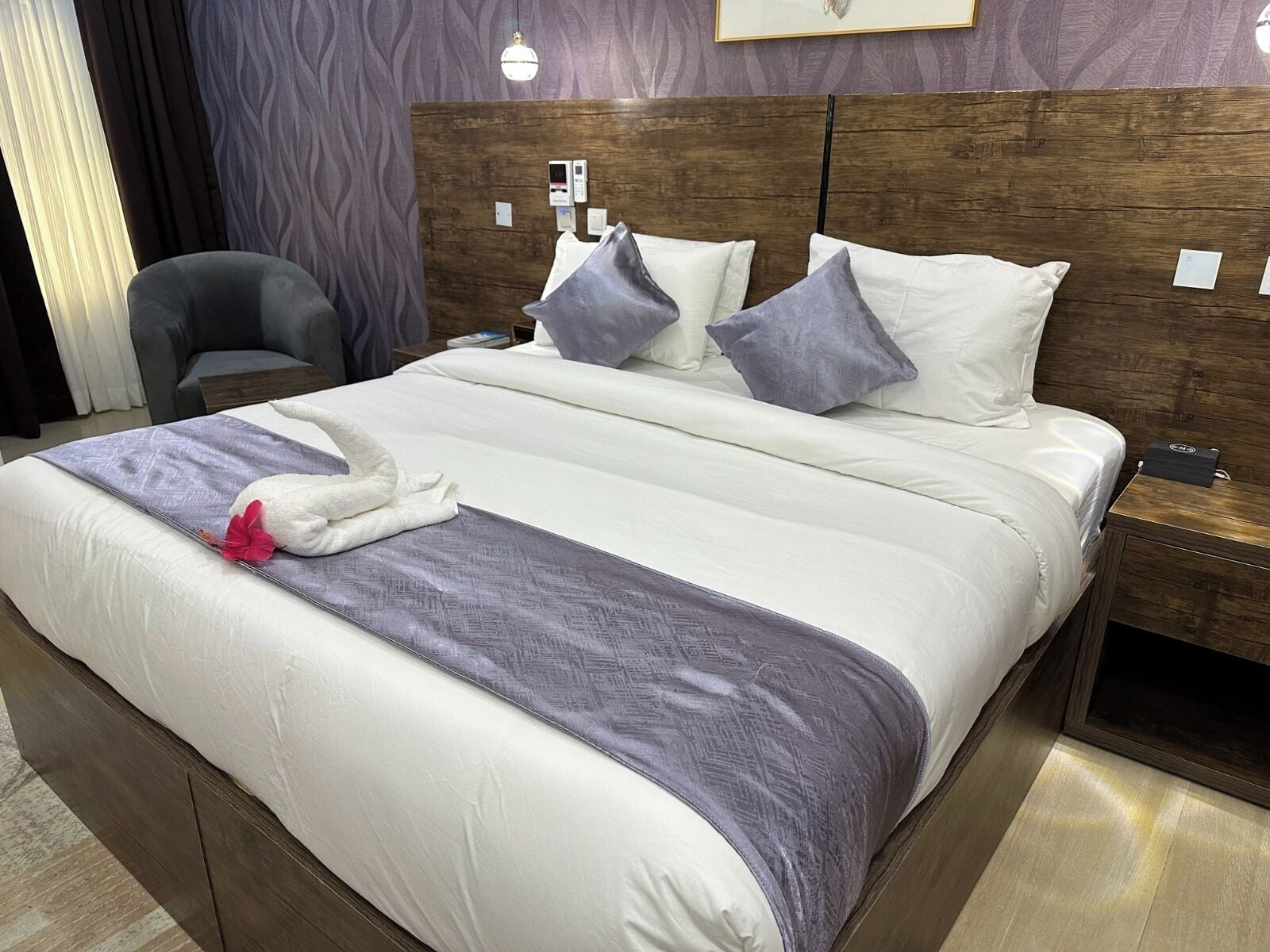 A neatly made bed with a white and purple bedspread, a decorative towel, and a pillow arrangement.
