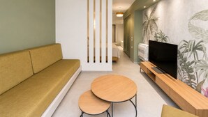 Ein modernes Wohnzimmer mit einer Couch, zwei runden Tischen, einem Fernseher und einer Wand mit einem tropischen Pflanzenwandbild.