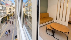 Ein modernes Interieur mit einer Couch und einem Tisch, Blick auf eine Straße mit Fußgängern und Häuser mit Balkonen.