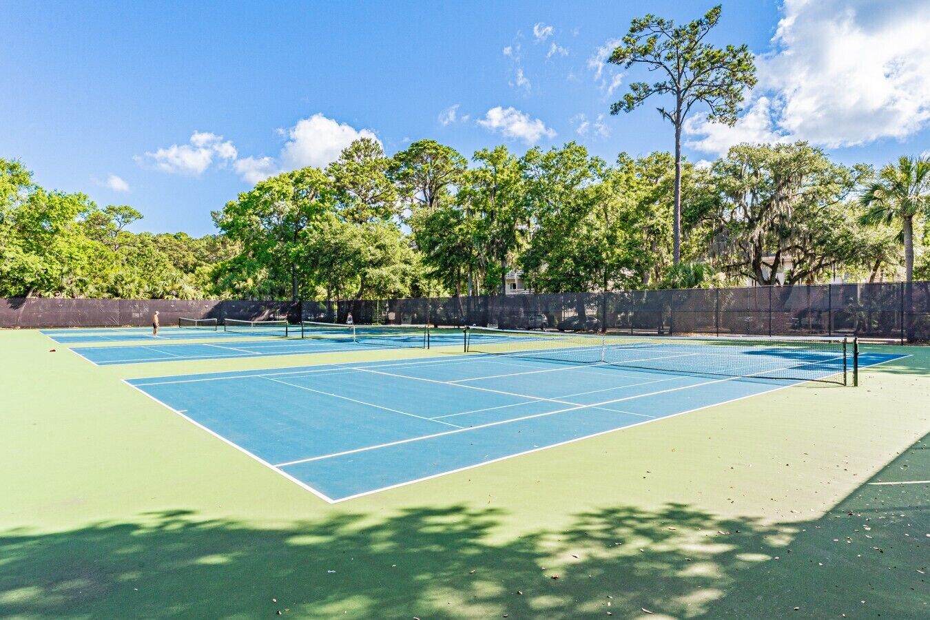 An outdoor tennis court with a net, surrounded by trees and a fence.