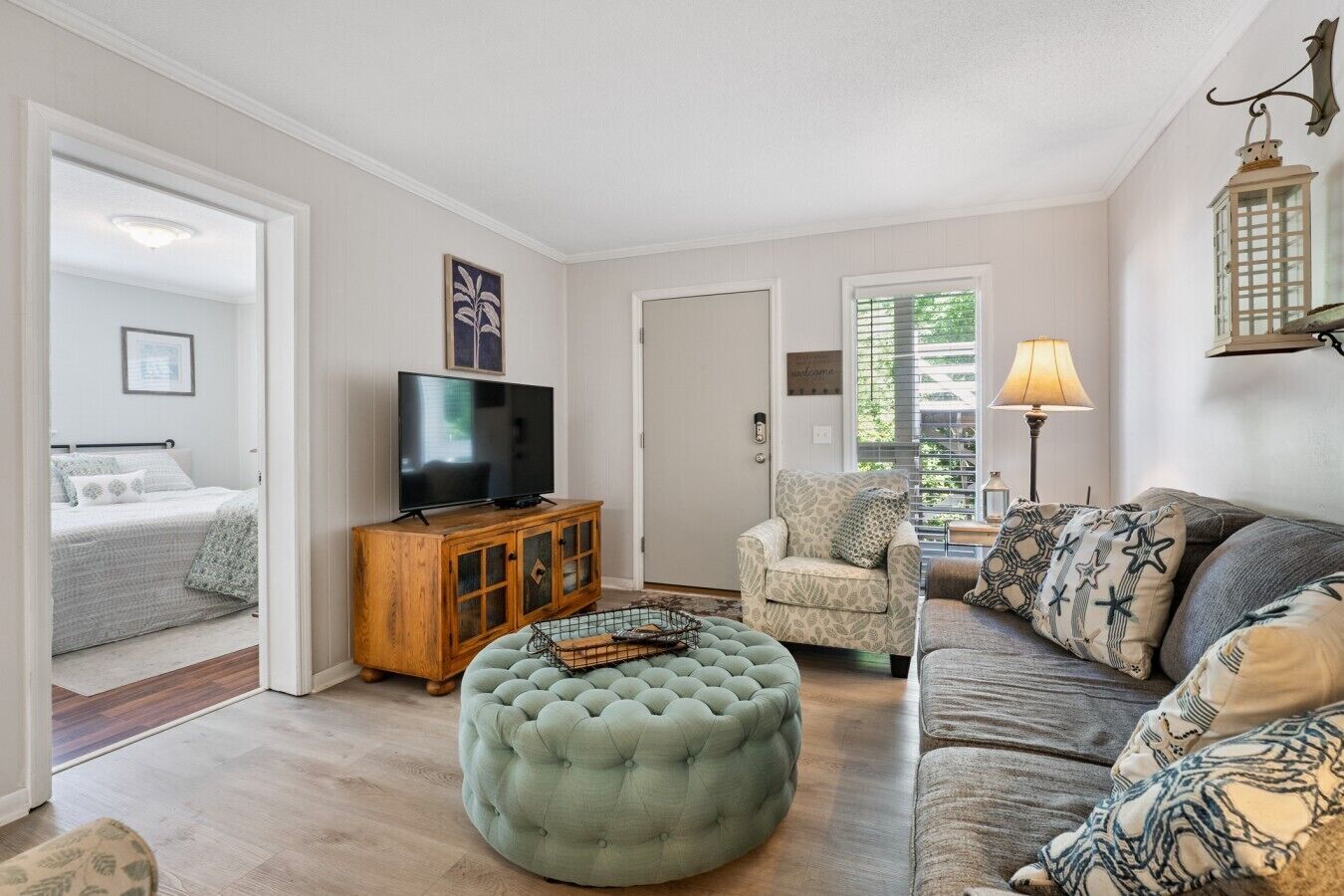 A living room with a television, ottoman, sofa, and armchair.