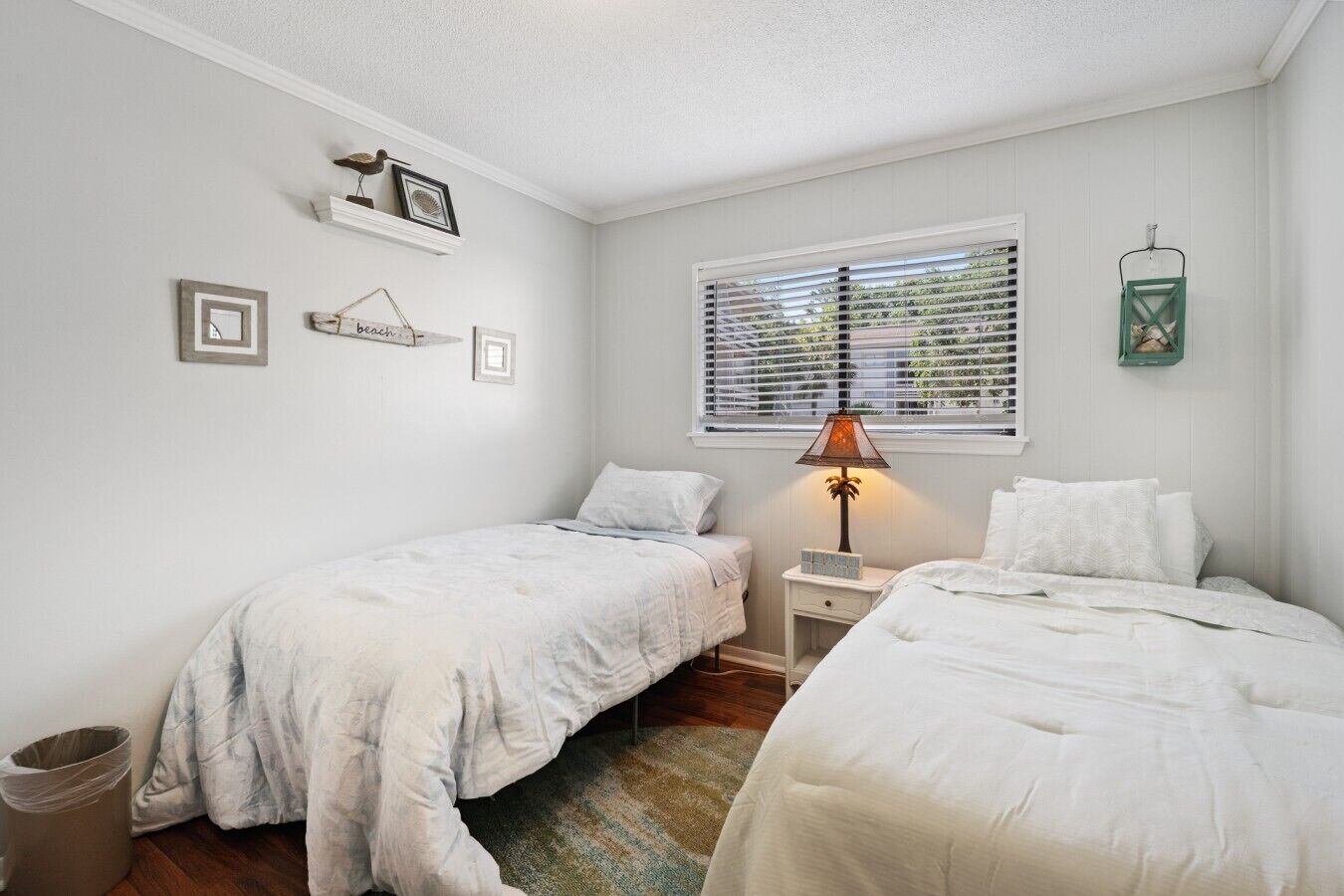 A bedroom with two beds, a window with blinds, a lamp, and wall decorations.