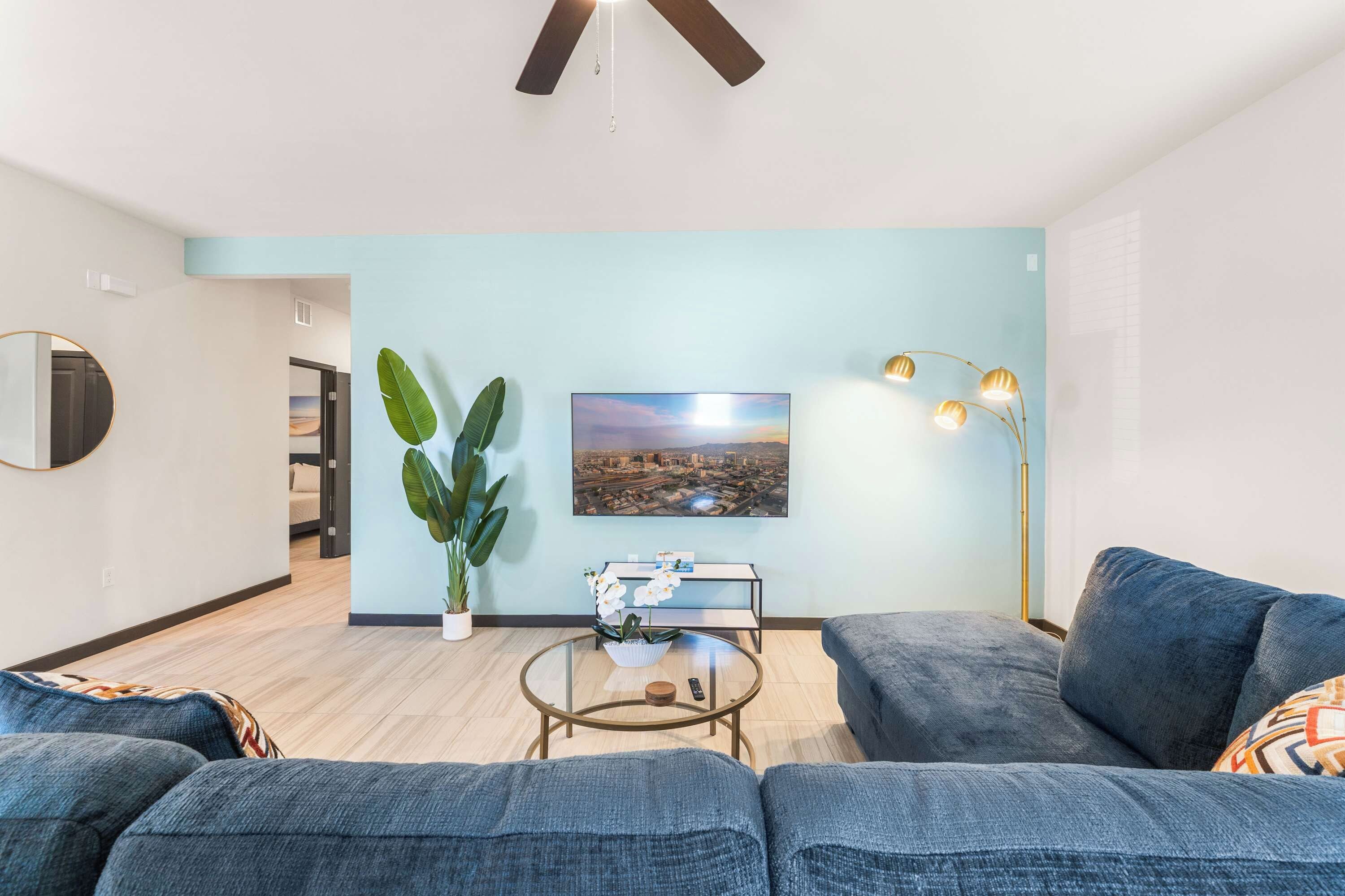 A modern living room with a sofa, a coffee table, a plant, and a cityscape painting.
