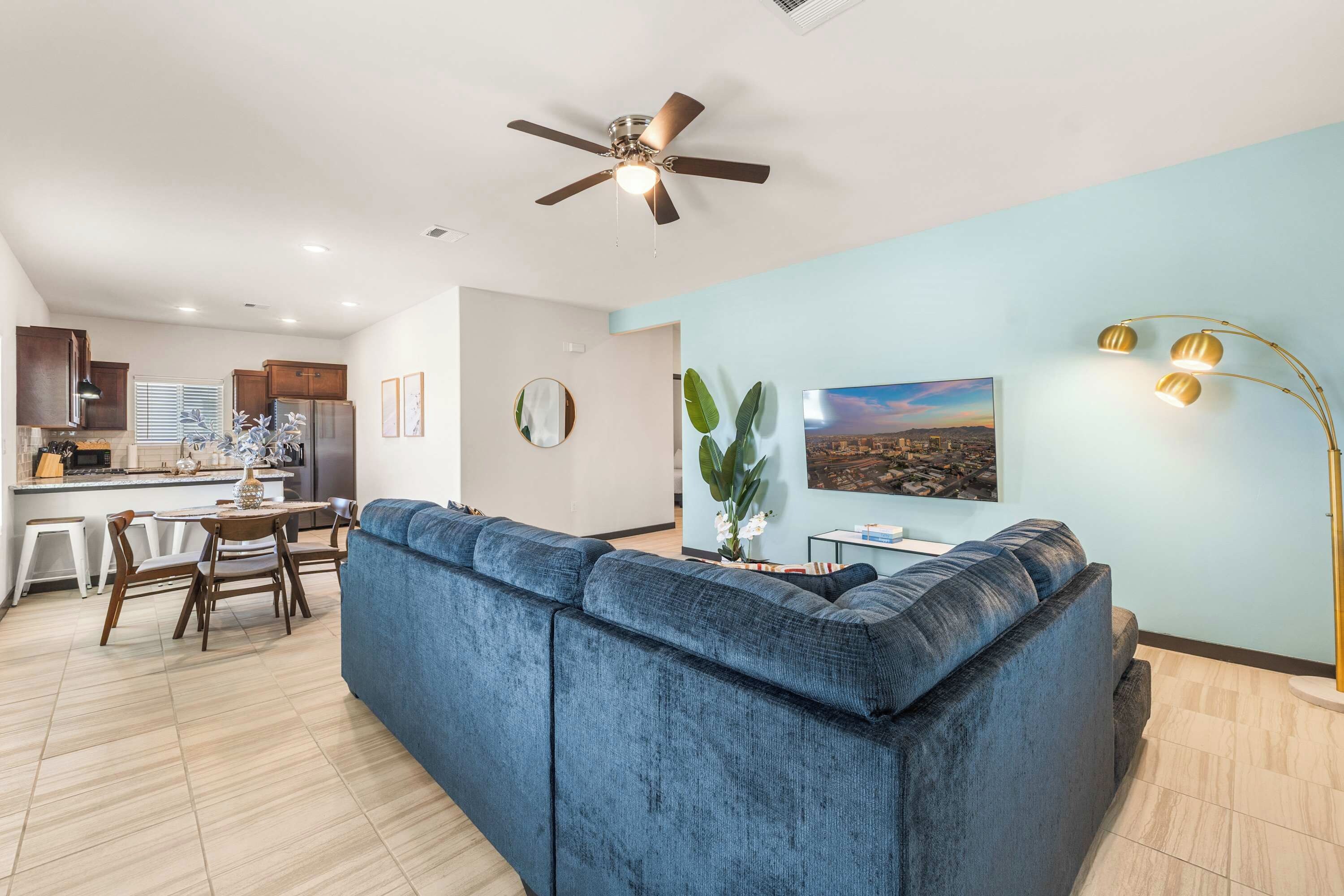 Ein modernes Wohnzimmer mit einem blauen Sofa, einem Essbereich mit Tisch und Stühlen, einer Küche mit Schränken und Geräten sowie einem Deckenventilator.