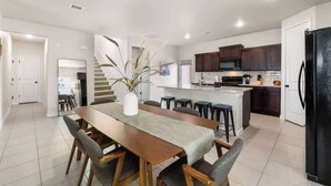 A modern kitchen with dark cabinets, a central island, and a dining area with a long wooden table and chairs.