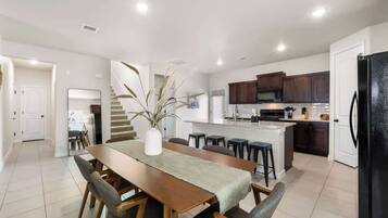 A modern kitchen with dark cabinets, a central island, and a dining area with a long wooden table and chairs.
