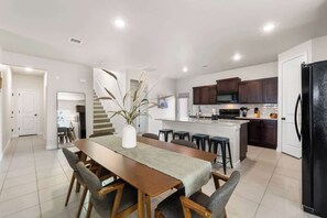 Une cuisine moderne avec des meubles de couleur sombre, un îlot central et un coin repas comprenant une longue table en bois et des chaises.