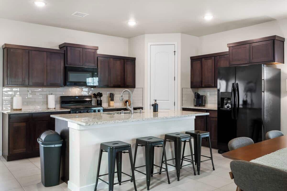 Una cucina moderna con mobili in legno scuro, un frigorifero in acciaio inossidabile, un'isola centrale con sgabelli e un backsplash in piastrelle bianche.