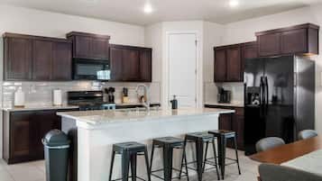 A modern kitchen with dark wooden cabinets, a stainless steel refrigerator, a central island with stools, and a white tiled backsplash.