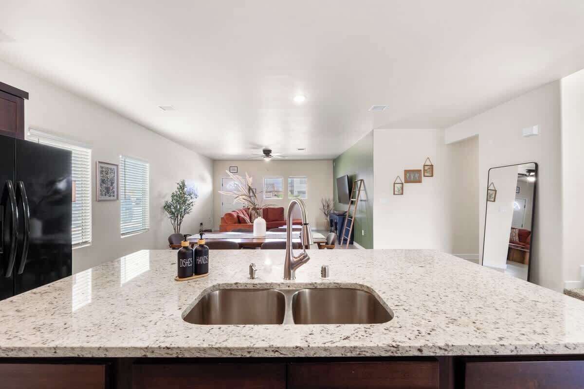 A kitchen with a granite countertop, stainless steel sink, and a refrigerator.