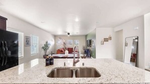 A kitchen with a granite countertop, stainless steel sink, and a refrigerator.